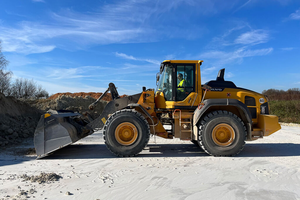 Excavadora amarilla trabajando en una obra al aire libre bajo un cielo azul con nubes.