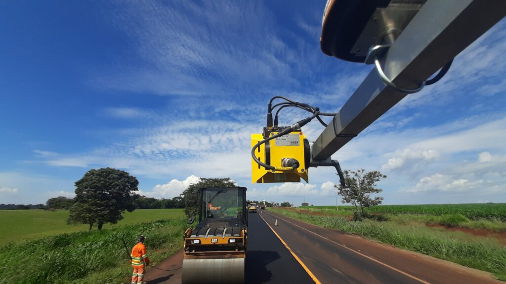 Tecnología PAVE-IR en la máquina pavimentadora, con una máquina de compactación de asfalto al fondo en un día de trabajo al aire libre.
